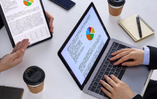 Hands reviewing compliance reports on a laptop and tablet